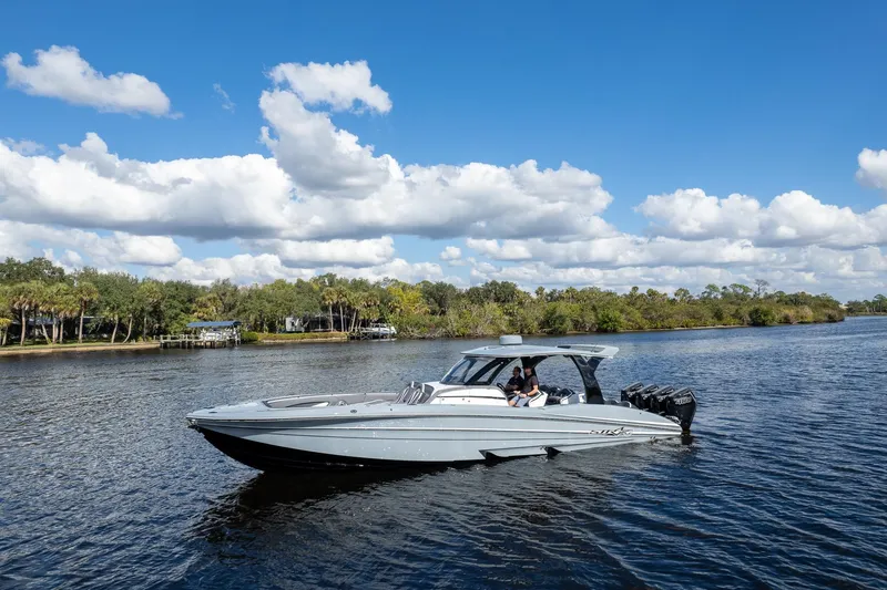  Yacht Photos Pics 2020 MTI V42 boat cruising on a scenic river under a blue sky with clouds.