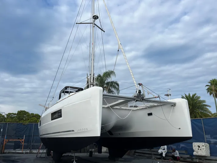  Yacht Photos Pics 2023 Lagoon 40 catamaran on land, under a cloudy sky, with palm trees in the background.