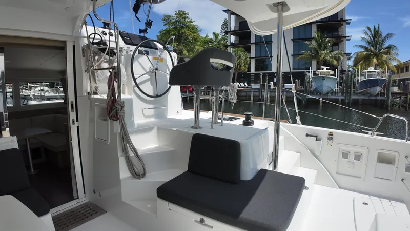  Yacht Photos Pics 2023 Lagoon 40 yacht cockpit with steering wheel, docked near modern buildings and palm trees.