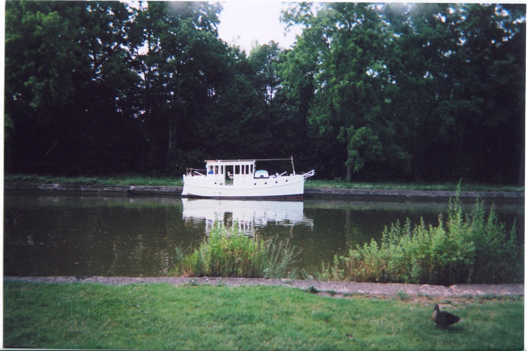 Custom 2005 sail-assisted trawler on a serene river, surrounded by lush greenery.