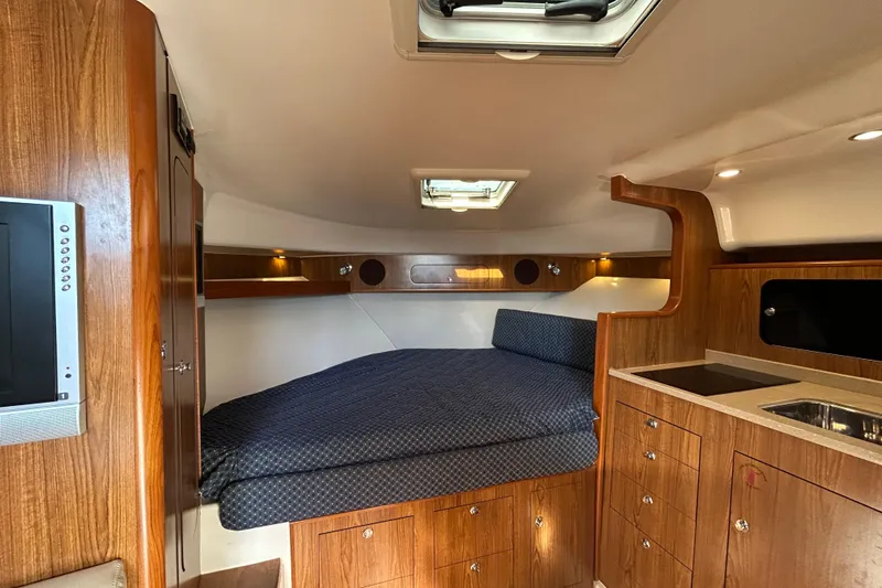  Yacht Photos Pics 2009 Pursuit OS 375 Offshore cabin interior with bed, wood cabinetry, and kitchenette.