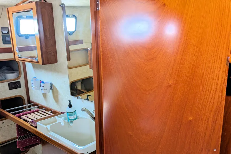 Iteration Yacht Photos Pics Interior of 1994 Amel 53 Super Maramu yacht bathroom with sink, mirror, and wooden cabinetry.