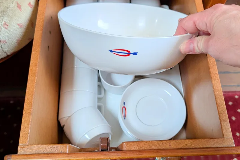 Iteration Yacht Photos Pics Hand holding a bowl with nautical emblem in a wooden drawer on Amel 53 Super Maramu, 1994.