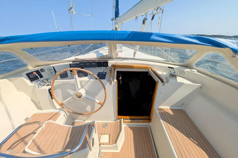 Iteration Yacht Photos Pics Cockpit of 1994 Amel 53 Super Maramu sailboat with wooden steering wheel and blue canopy.