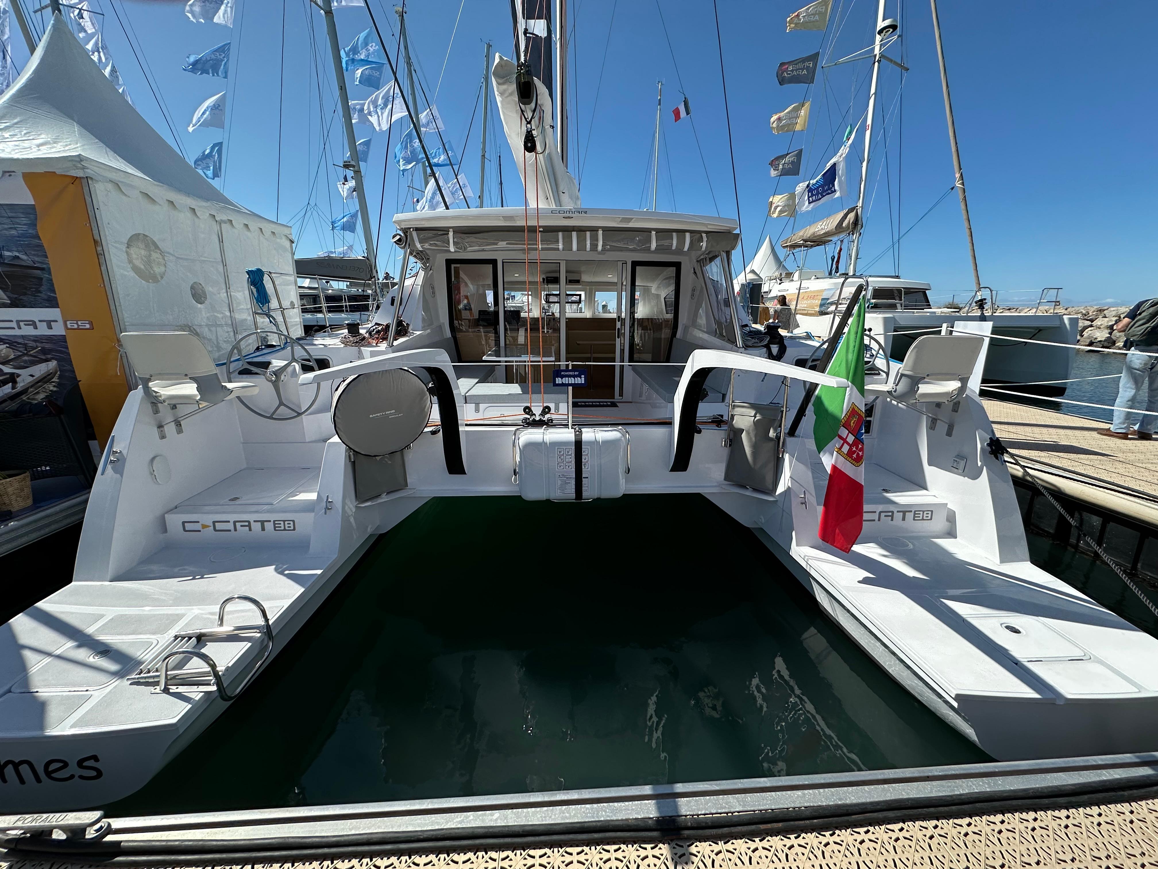 2025 Comar C-Cat 38 Catamaran docked at marina, rear view with flags and clear sky.