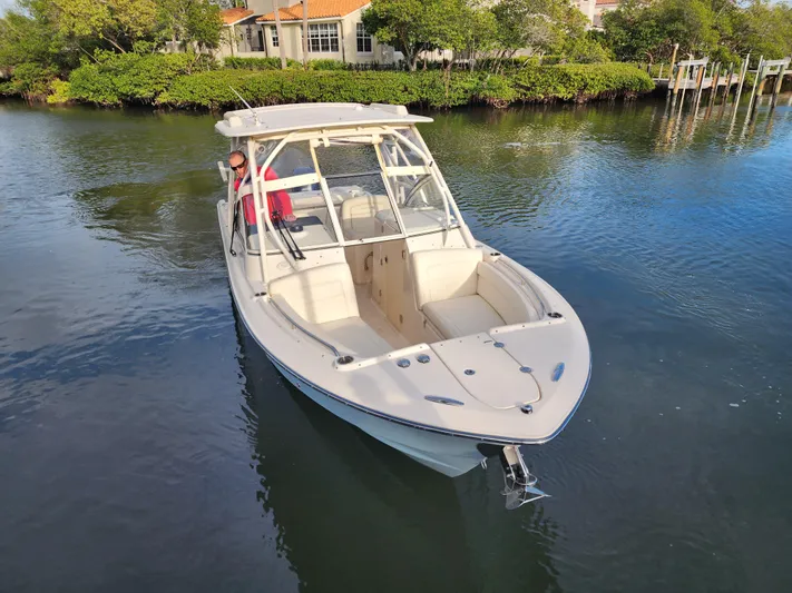  Yacht Photos Pics 2023 Grady-White Freedom 275 boat on calm water, surrounded by lush greenery.