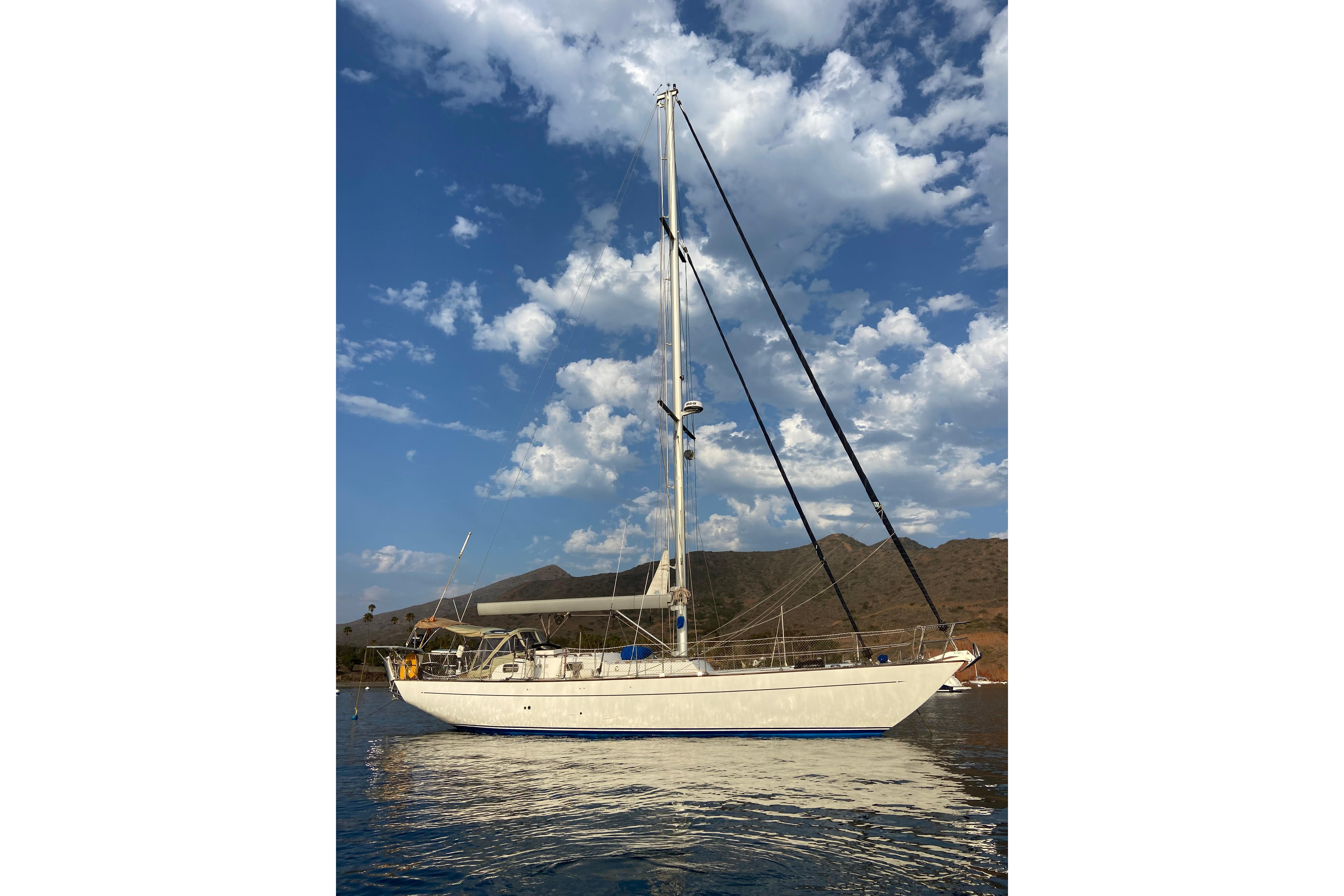 Sailboat Reliance 44, 1988 model, anchored with scenic mountain backdrop and cloudy sky.