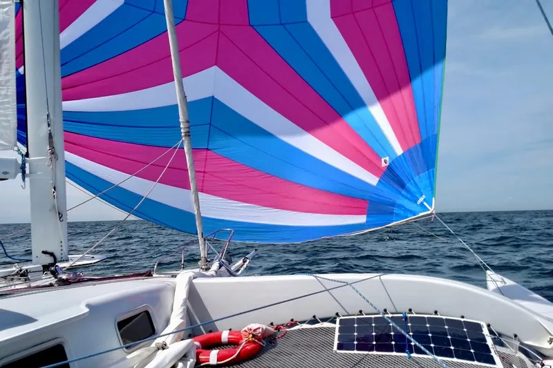 Wingnut Yacht Photos Pics Sailboat with colorful spinnaker sail on open sea, featuring solar panels on deck.