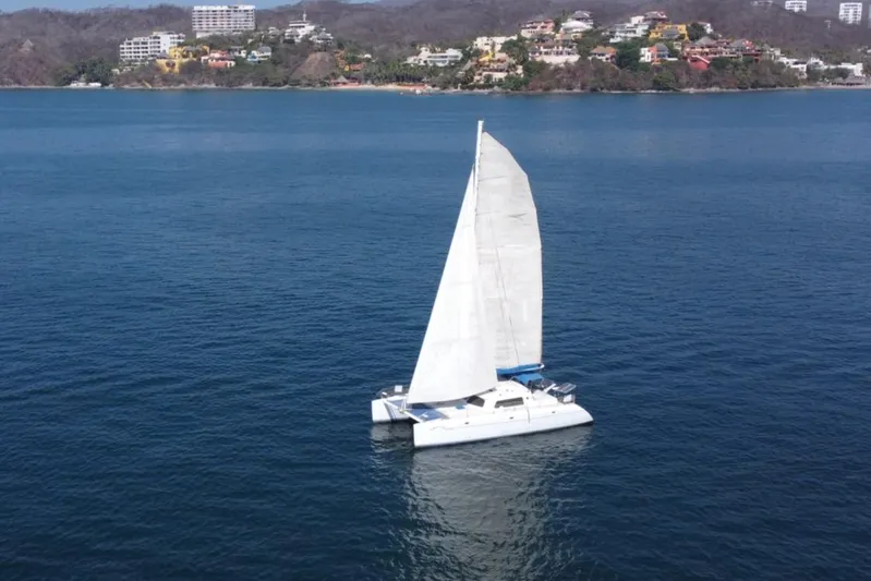 Capricorn Cat Yacht Photos Pics Sailing catamaran "Kurt Hughes 45" on calm blue waters, coastal backdrop, 1995 model.