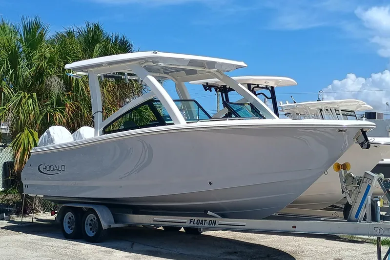 257-155 Yacht Photos Pics 2025 Robalo R257 Dual Console boat on trailer, parked near palm trees under blue sky.