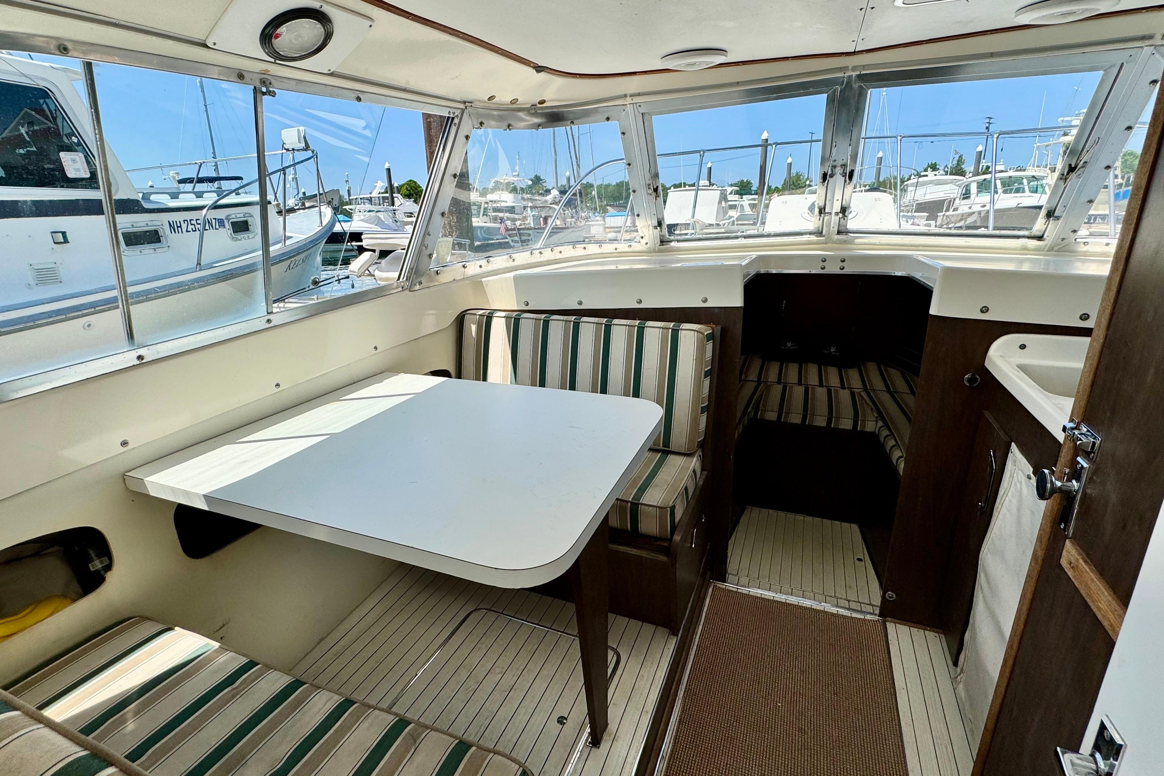1973 Bertram 31 Flybridge Cruiser interior with striped seating and table, docked at marina.