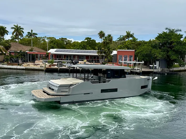  Yacht Photos Pics 2023 De Antonio Yachts D50 Coup&eacute; cruising near waterfront homes, surrounded by lush greenery.