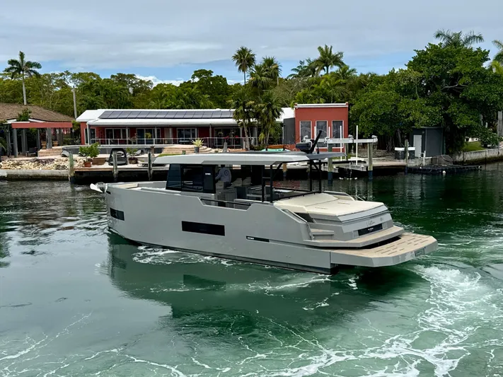  Yacht Photos Pics 2023 De Antonio Yachts D50 Coup&eacute; cruising near a waterfront property with lush greenery.