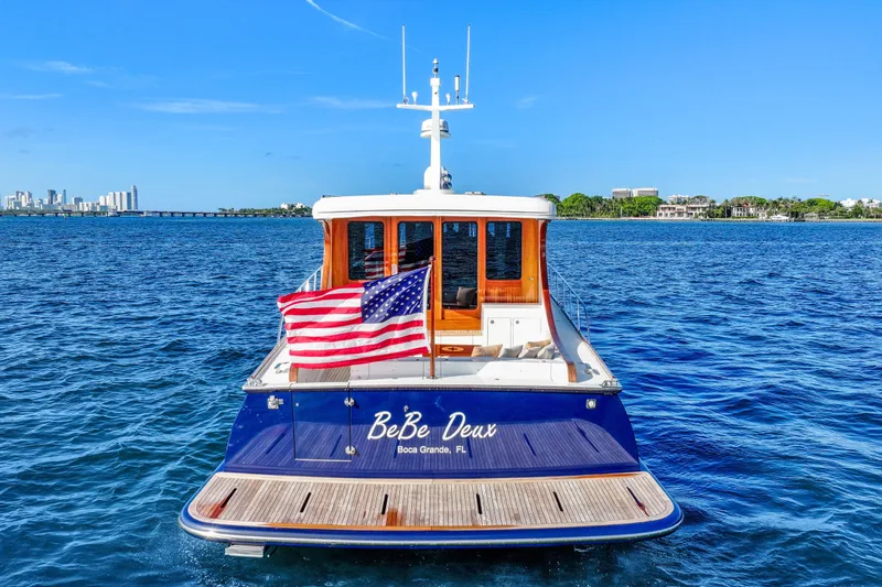 Bebe Deux Yacht Photos Pics 2023 Vicem 65 Classic yacht on water, American flag, city skyline in background.