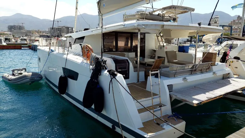  Yacht Photos Pics 2018 Fountaine Pajot Saona 47 catamaran docked in a marina, with mountains in the background.