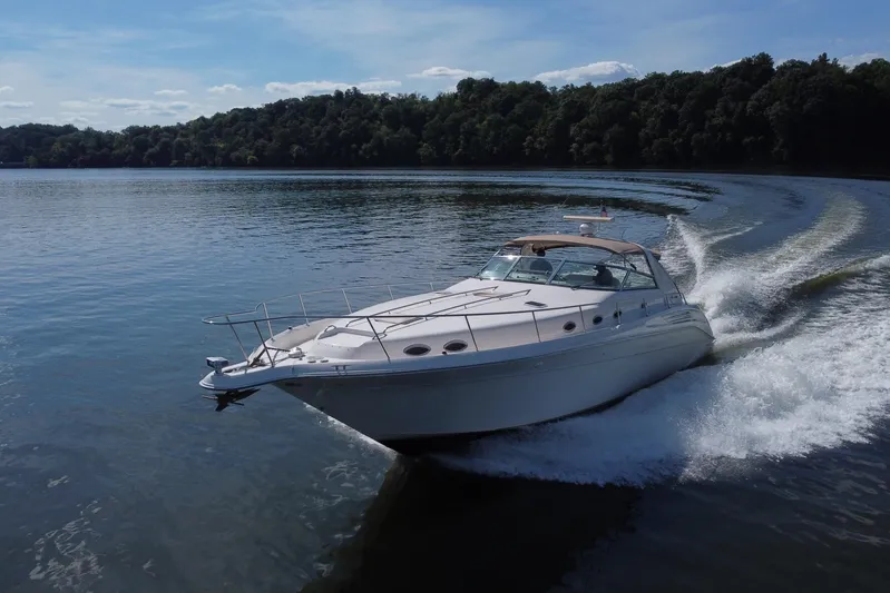  Yacht Photos Pics 1997 Sea Ray 450 Sundancer cruising on a serene lake with lush forest backdrop.