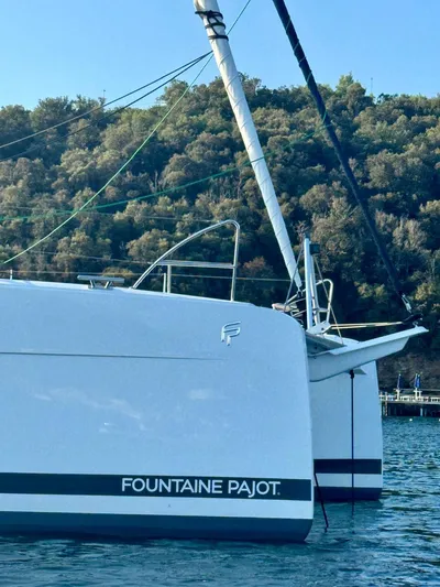  Yacht Photos Pics 2024 Fountaine Pajot Catamaran Elba 45 on serene water with lush hillside backdrop.