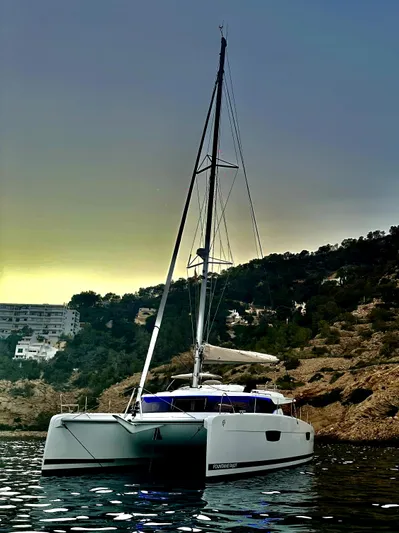  Yacht Photos Pics 2024 Fountaine Pajot Elba 45 catamaran sailing near rocky coastline at sunset.