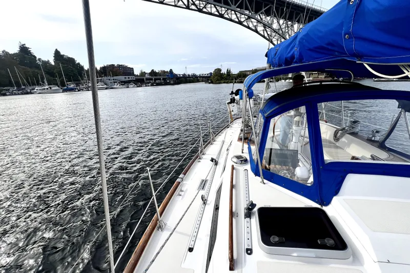  Yacht Photos Pics 1989 Taswell 43 sailboat cruising under a bridge, featuring blue canopy and scenic waterfront.