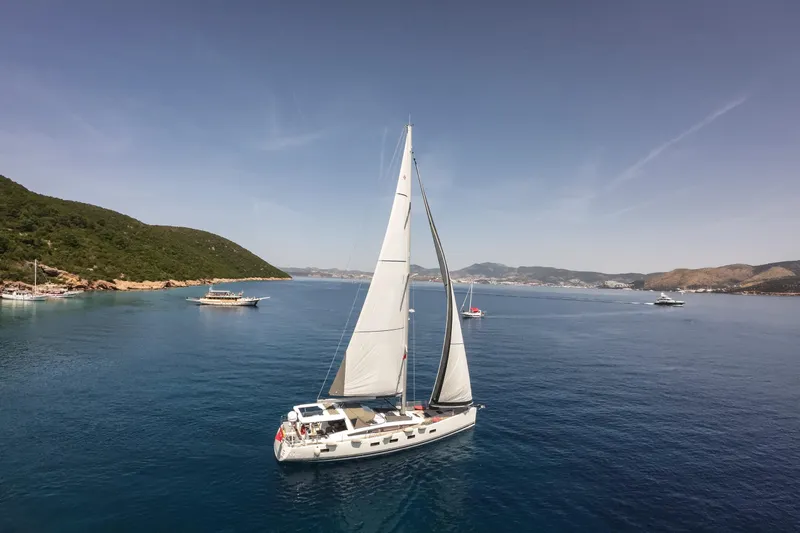  Yacht Photos Pics 2020 Jeanneau 64 sailing in a serene coastal bay with clear blue waters.