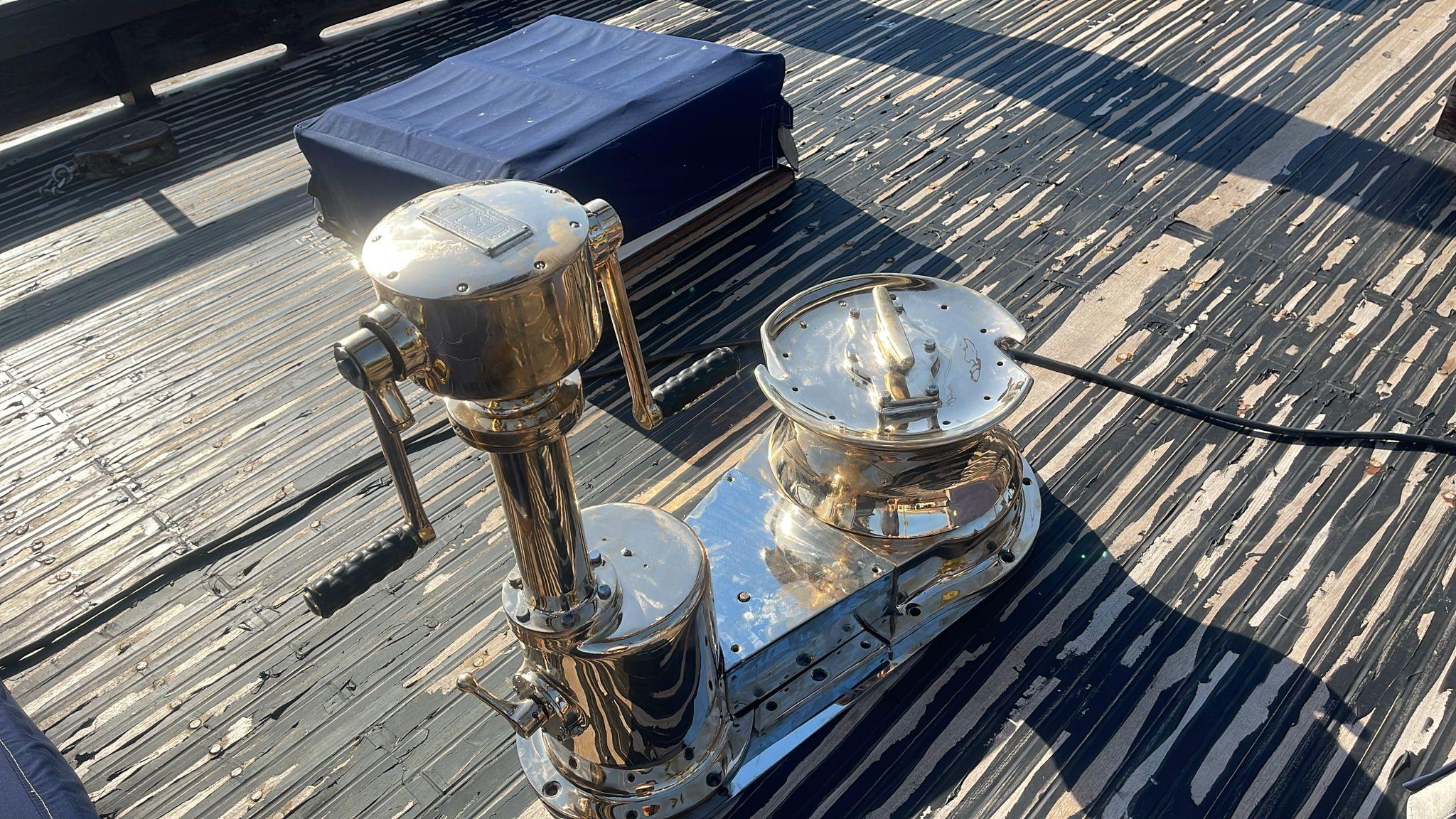 Polished winch on 1991 Horacio Carabelli Schooner deck, with blue cushion nearby.