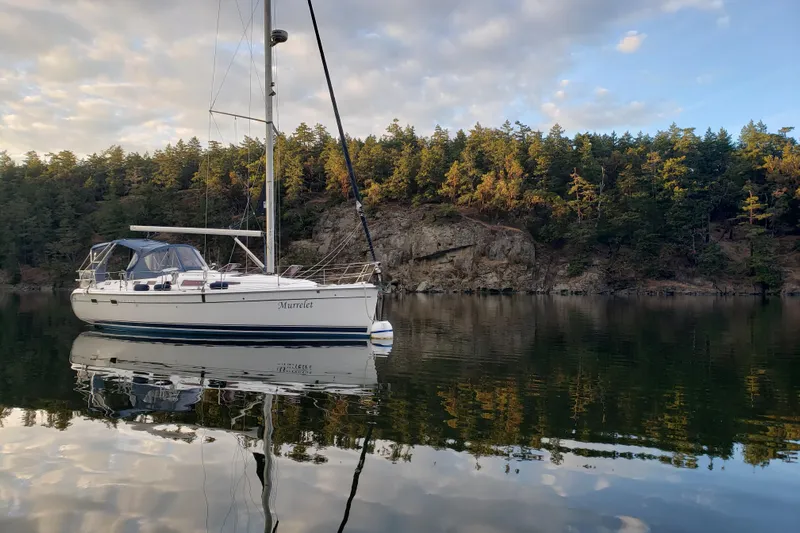 Murrelet Yacht Photos Pics Sailboat "Murrelet" on calm water, surrounded by forested cliffs, under a partly cloudy sky.