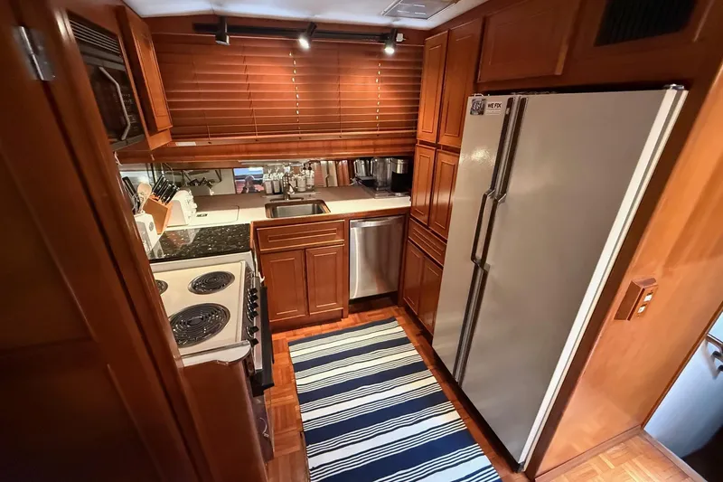 Sweet Caroline Yacht Photos Pics 1989 Jefferson Marquessa 52 yacht kitchen with wooden cabinets, modern appliances, and striped rug.