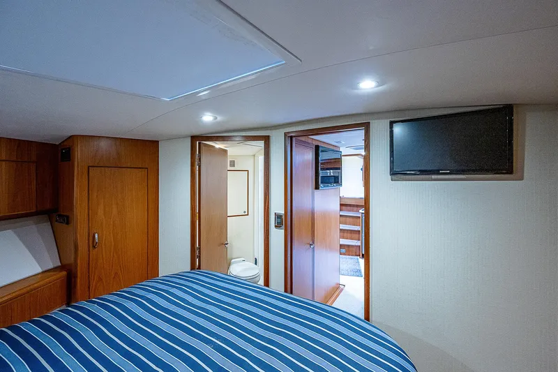 Wanted Yacht Photos Pics Interior of 2012 Cabo 44 HTX yacht bedroom with striped bedding and wall-mounted TV.