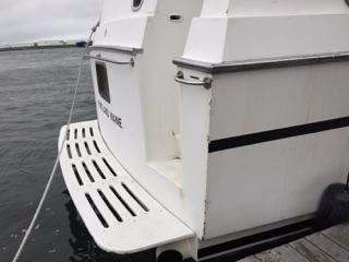 1990 Hi-Tech motor yacht stern view with swim platform, docked by the water.