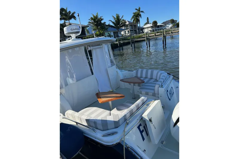 Fifth Child Yacht Photos Pics 2019 Back Cove 34O boat with striped seating and wooden tables, docked by palm trees.