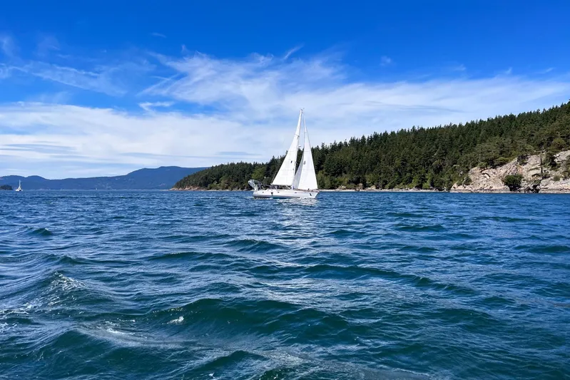 Misty Blue Yonder Yacht Photos Pics Sailboat Jeanneau Sun Odyssey 45.1 cruising on blue waters near forested coastline, under clear sky.