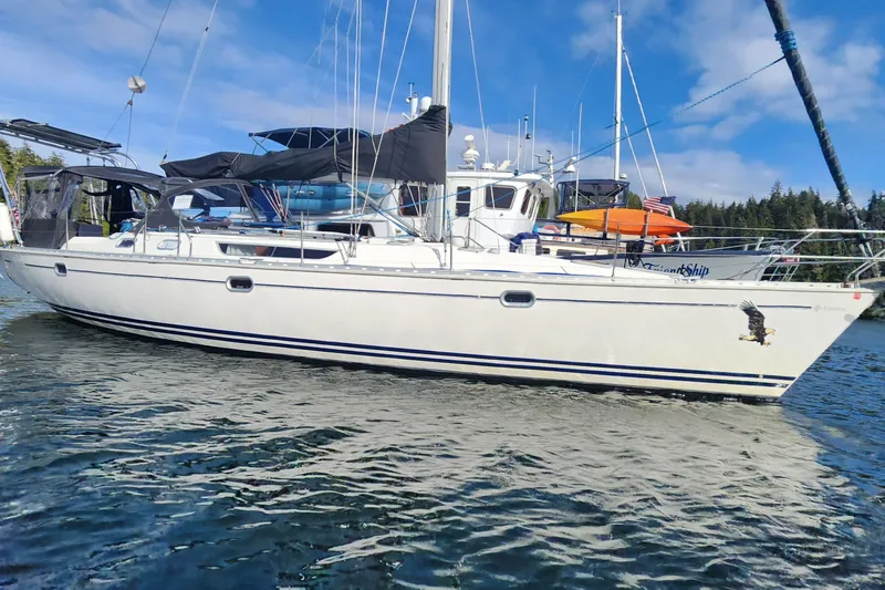Misty Blue Yonder Yacht Photos Pics 1995 Jeanneau Sun Odyssey 45.1 sailboat on water, with clear sky and forested background.