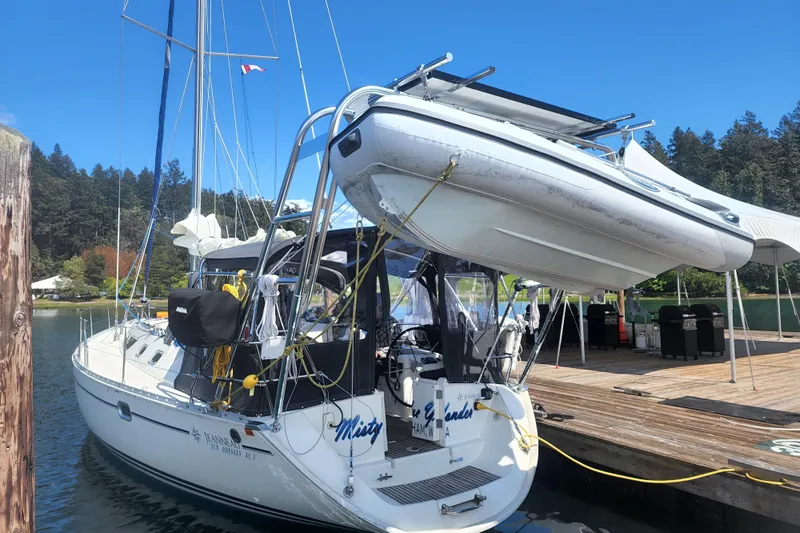 Misty Blue Yonder Yacht Photos Pics 1995 Jeanneau Sun Odyssey 45.1 sailboat docked with dinghy, surrounded by trees and clear sky.