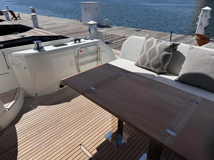  Yacht Photos Pics 2023 Prestige 520 F-Line yacht deck with wooden table and cushioned seating by the water.