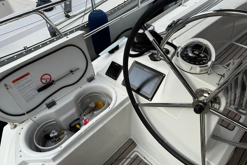Shaboom Yacht Photos Pics 2017 Jeanneau Sun Odyssey 479 cockpit with steering wheel, compass, and open storage compartment.