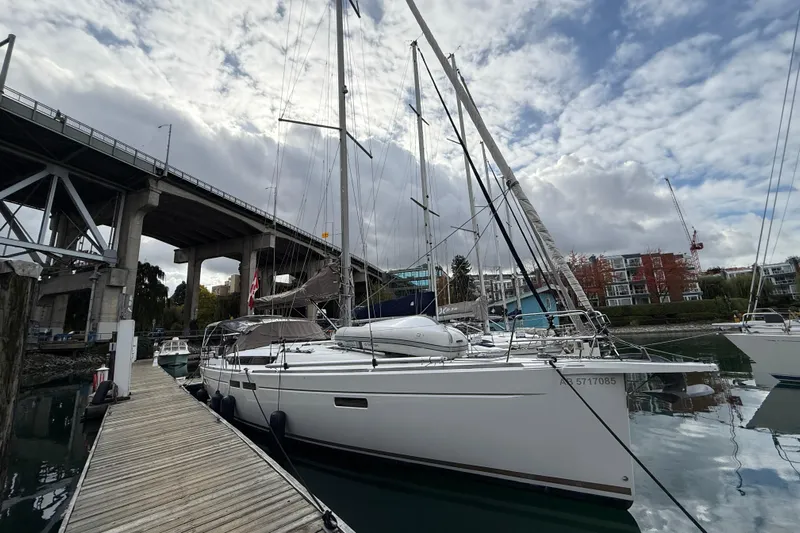 Shaboom Yacht Photos Pics 2017 Jeanneau Sun Odyssey 479 sailboat docked under a bridge, cloudy sky background.