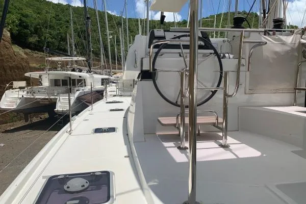 Never Say Never Yacht Photos Pics 2017 Lagoon 42 catamaran docked, showcasing deck and steering wheel, with lush greenery in background.
