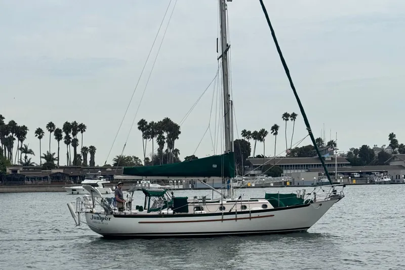 Juniper Yacht Photos Pics 1988 Pacific Seacraft 34 sailboat on calm water, with palm trees in the background.