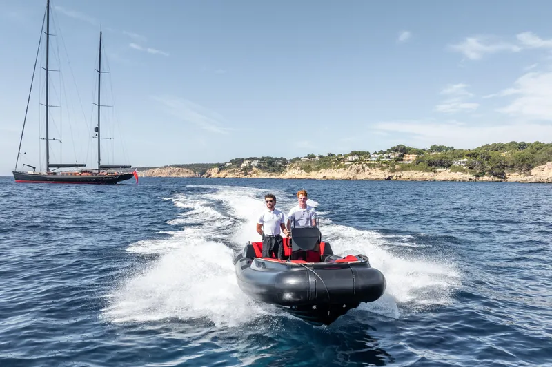 Maximus Yacht Photos Pics Two people on a speedboat near a 2023 Vitters Cruising Ketch, coastal background.