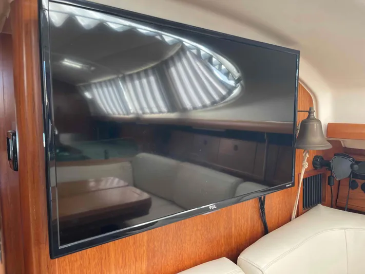 No Agenda Yacht Photos Pics Flat-screen TV in 2003 Jeanneau Deck Salon interior, wooden paneling, and beige seating.