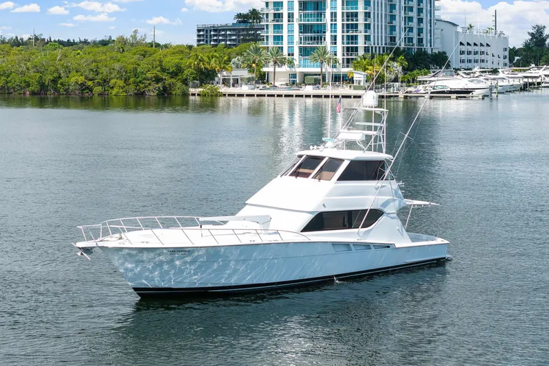 Sand Control Yacht Photos Pics 2002 Hatteras 60 Convertible yacht on calm water near a marina and modern buildings.