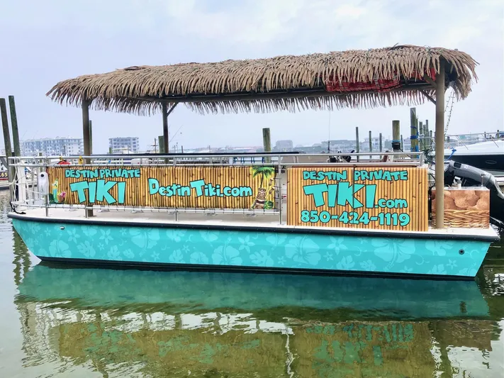 Big Kahuna Yacht Photos Pics Tiki-themed 2022 Beachcat COI Tiki Boat with bamboo decor and thatched roof on calm water.