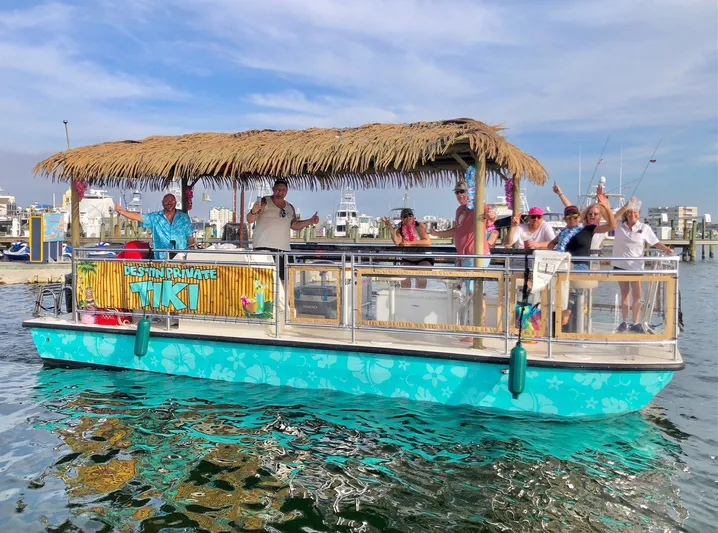 Big Kahuna Yacht Photos Pics 2022 Beachcat COI Tiki Boat with passengers, featuring a thatched roof, on a sunny day.