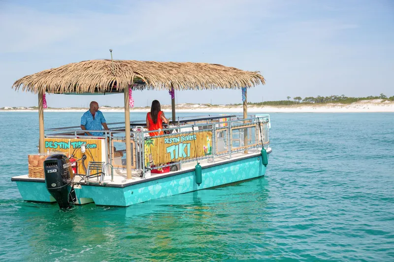 Big Kahuna Yacht Photos Pics 2022 Beachcat COI Tiki Boat on turquoise water with thatched roof and passengers.