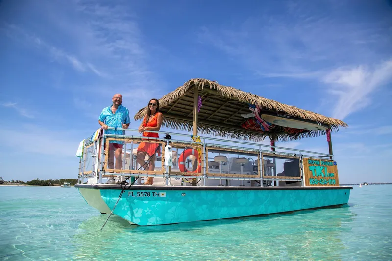 Big Kahuna Yacht Photos Pics 2022 Beachcat COI Tiki Boat on clear water, featuring a thatched roof and vibrant design.