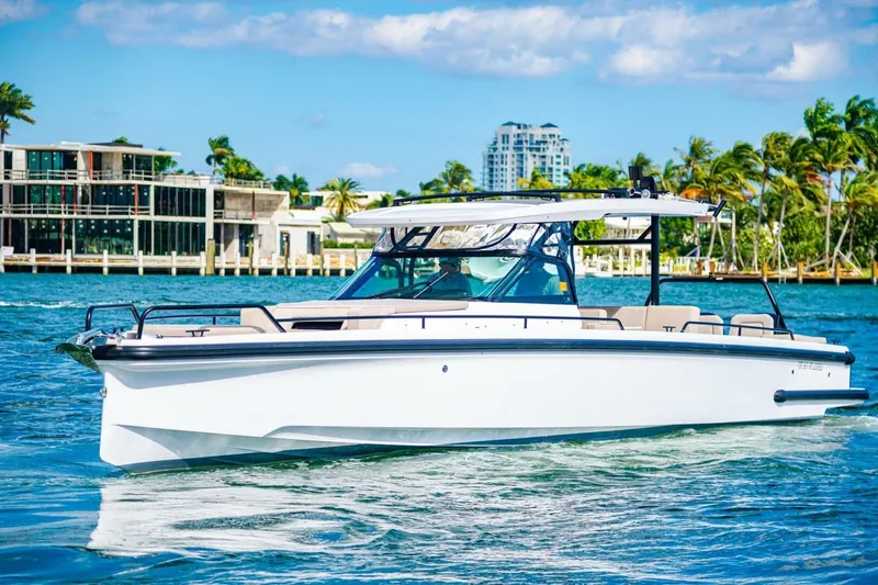 First Byte Yacht Photos Pics 2023 Axopar 37 Sun Top boat cruising on a sunny day near modern waterfront buildings.