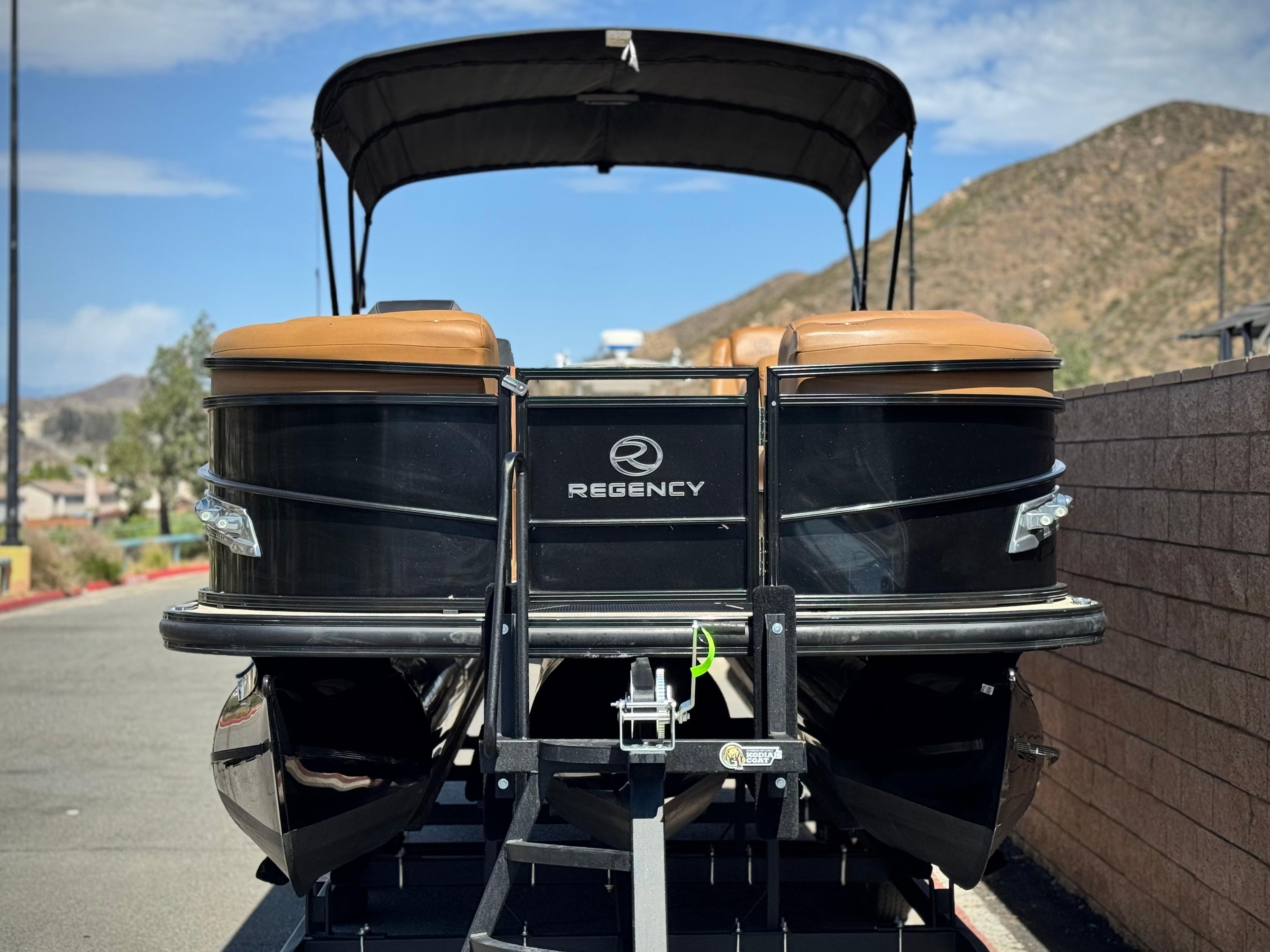 2021 Regency 230 LE3 pontoon boat on trailer, parked outdoors with scenic mountain backdrop.