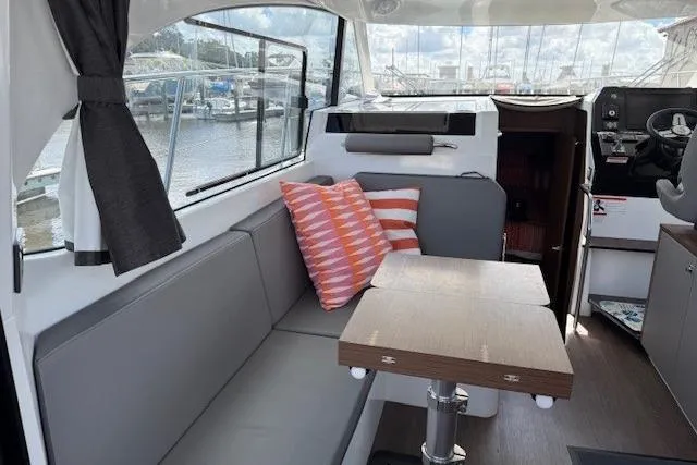 Venture Yacht Photos Pics 2024 Beneteau Antares 11 interior with gray seating, wooden table, and striped cushions.