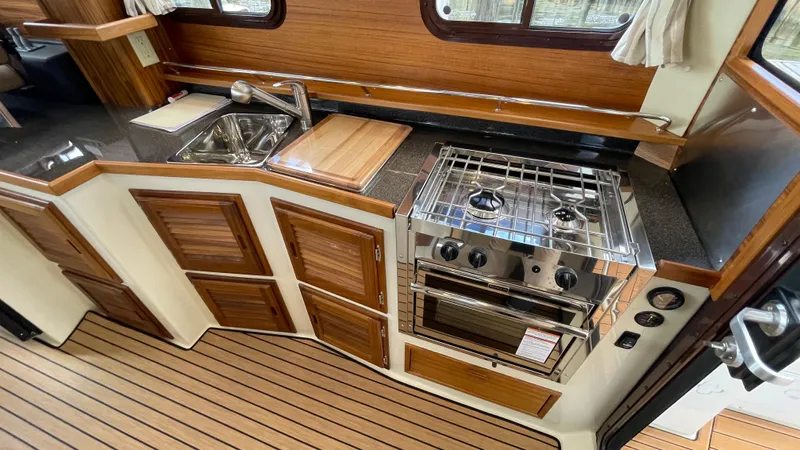  Yacht Photos Pics 2023 Ranger Tugs R-31 CB kitchen with stove, sink, and wooden cabinetry.