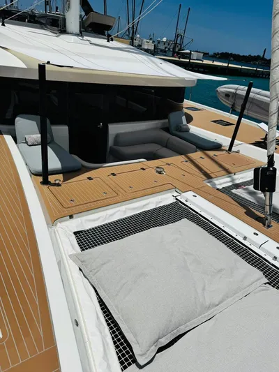  Yacht Photos Pics 2024 Lagoon 65 yacht deck with cushioned seating and netting, docked in a marina.